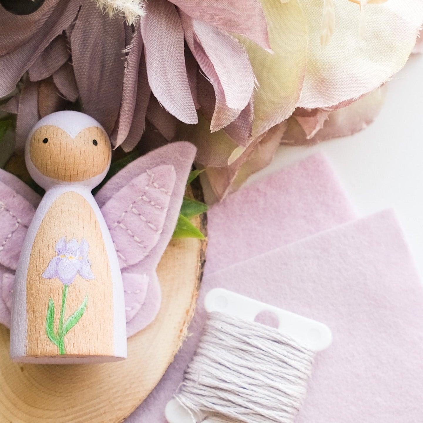 Wooden fairy figurine with purple wings and purple Iris painted, doll is places on a wooden surface with flowers and berries.